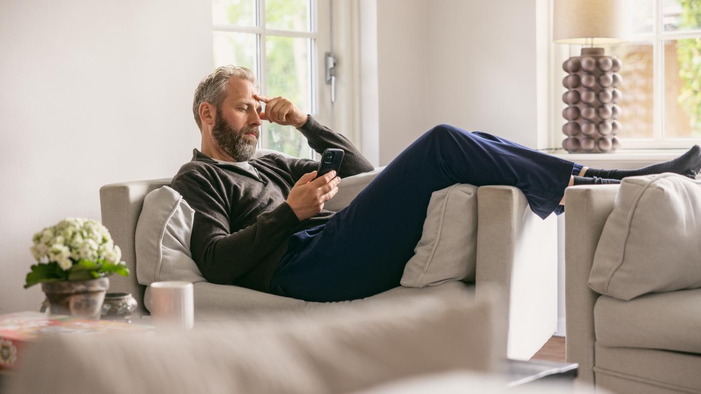 Mand ligger i sofaen med sin mobiltelefon
