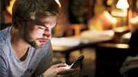 Mand kigger på mobiltelefon i dæmpet belysning. Han tjekker sit aktiedepot i mobilbanken