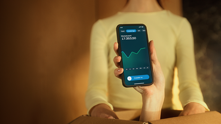 Hånd med mobiltelefon, der viser investeringskonto i Danske Banks mobilbank