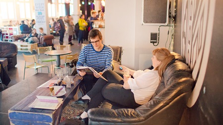 Two friends at coffee shop studying and talking while hanging out in the sofa