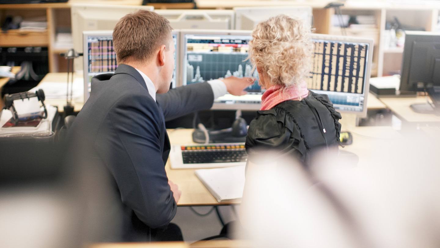 mand og kvinde kigger på aktiekurser på skærm