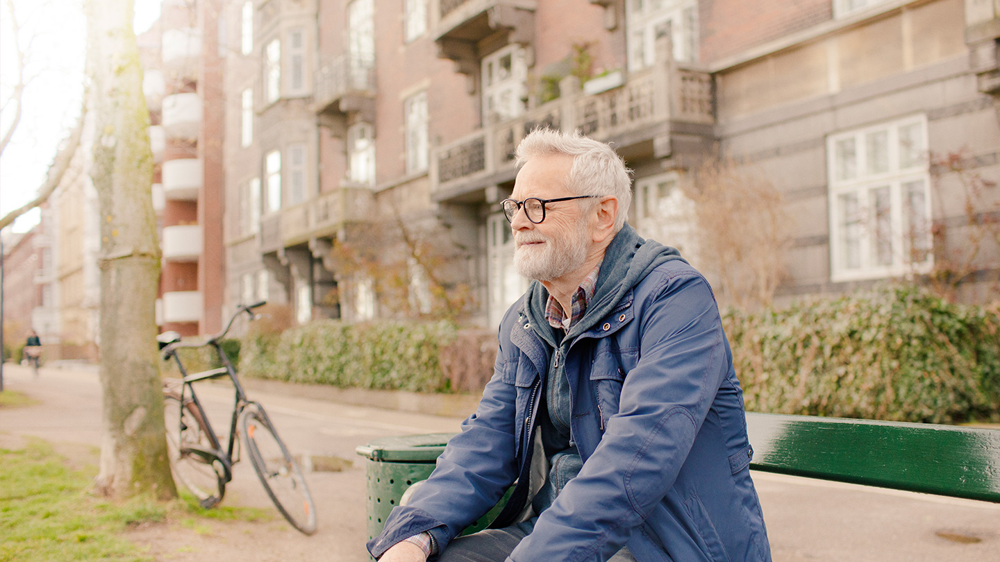 Mand der sidder på en bænk foran bygning